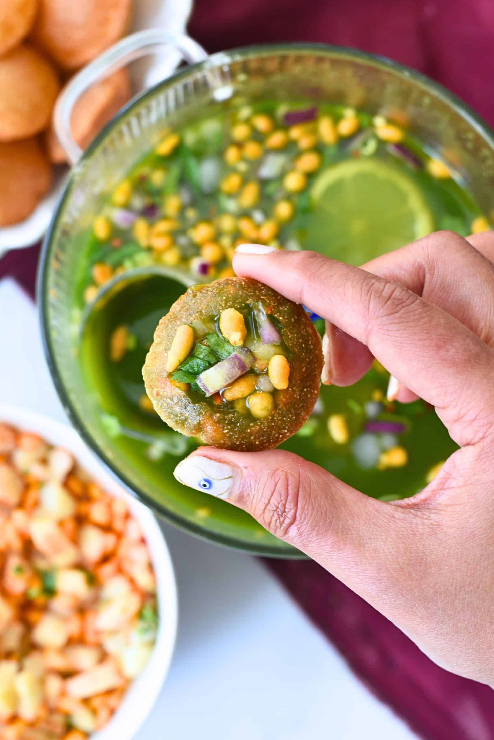 holding spicy pani puri with tangy , sweet pani in background.