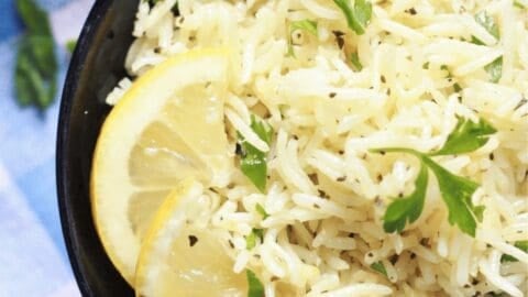 Lemon rice cooked with herbs in a bowl with lemon wedges