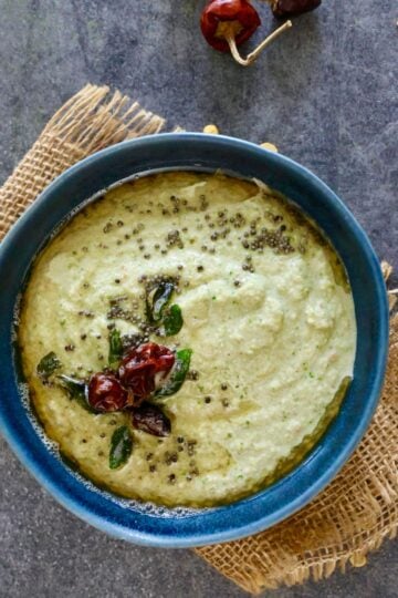 Green curry soup with herbs and spices in a blue bowl.