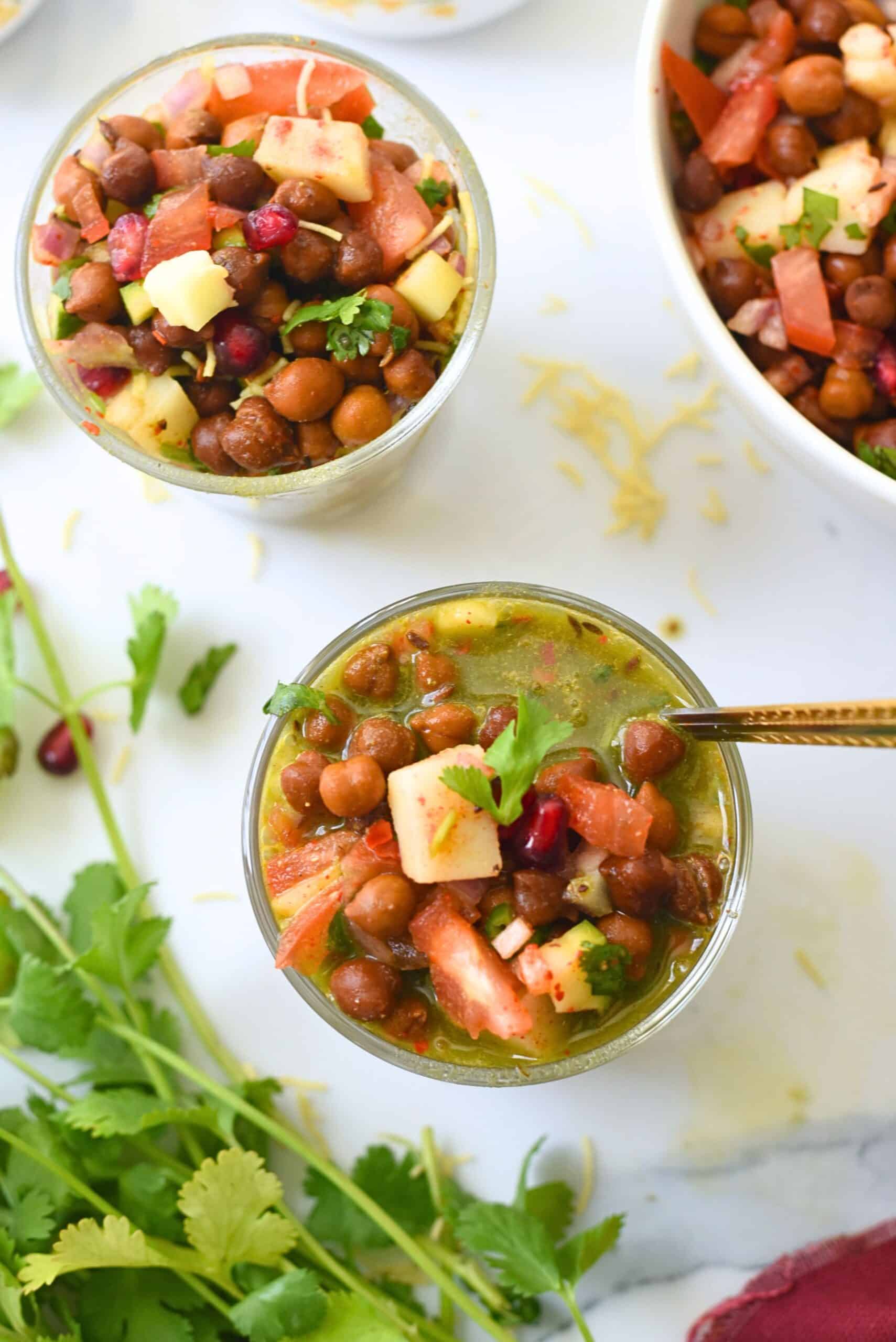 Close-up of kala chana chaat in a glass with fresh herbs and vegetables.