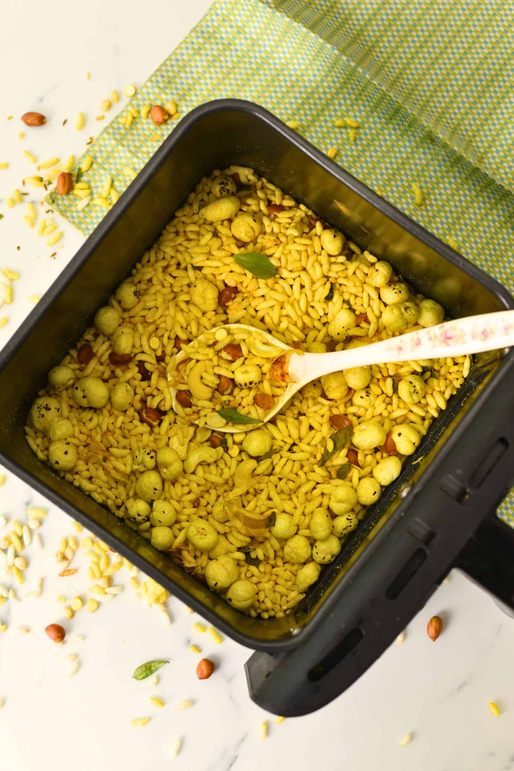 Masala murmura chivda in an air fryer basket, showing spiced puffed rice mixed with peanuts, chana dal, and curry leaves, lightly roasted and crispy.