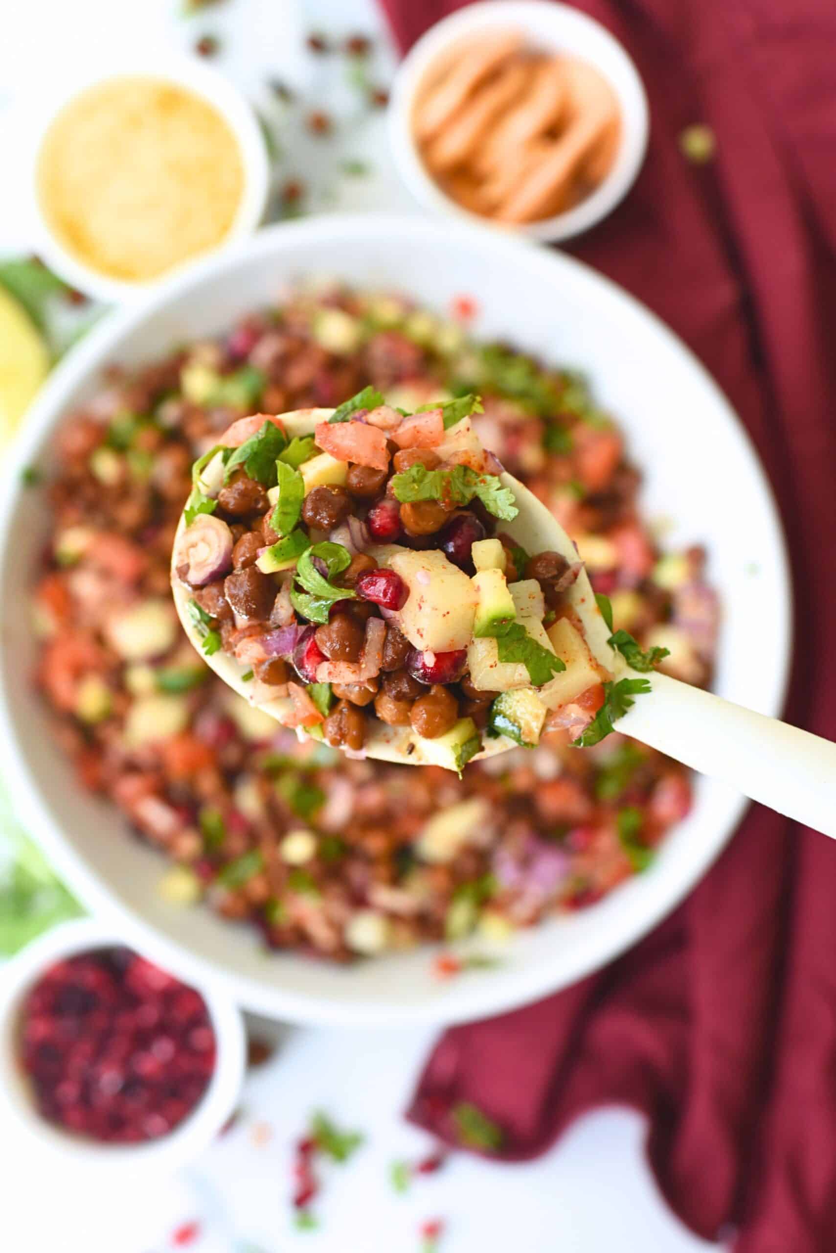 Close-up of kala chana chaat with chopped vegetables and spices in a spoon.