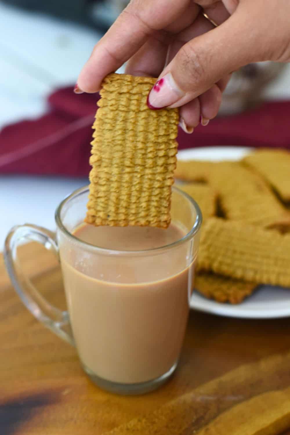 Hand dipping crispy Punjabi atta biscuit into a glass of tea.