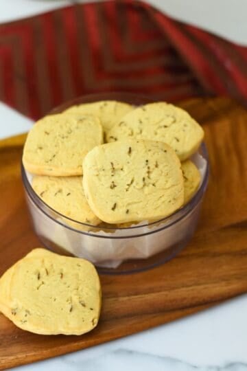 Close-up of homemade jeera biscuits in a glass bowl on wooden tray.
