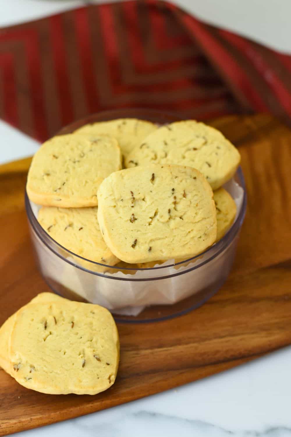 Close-up of homemade jeera biscuits in a glass bowl on wooden tray.