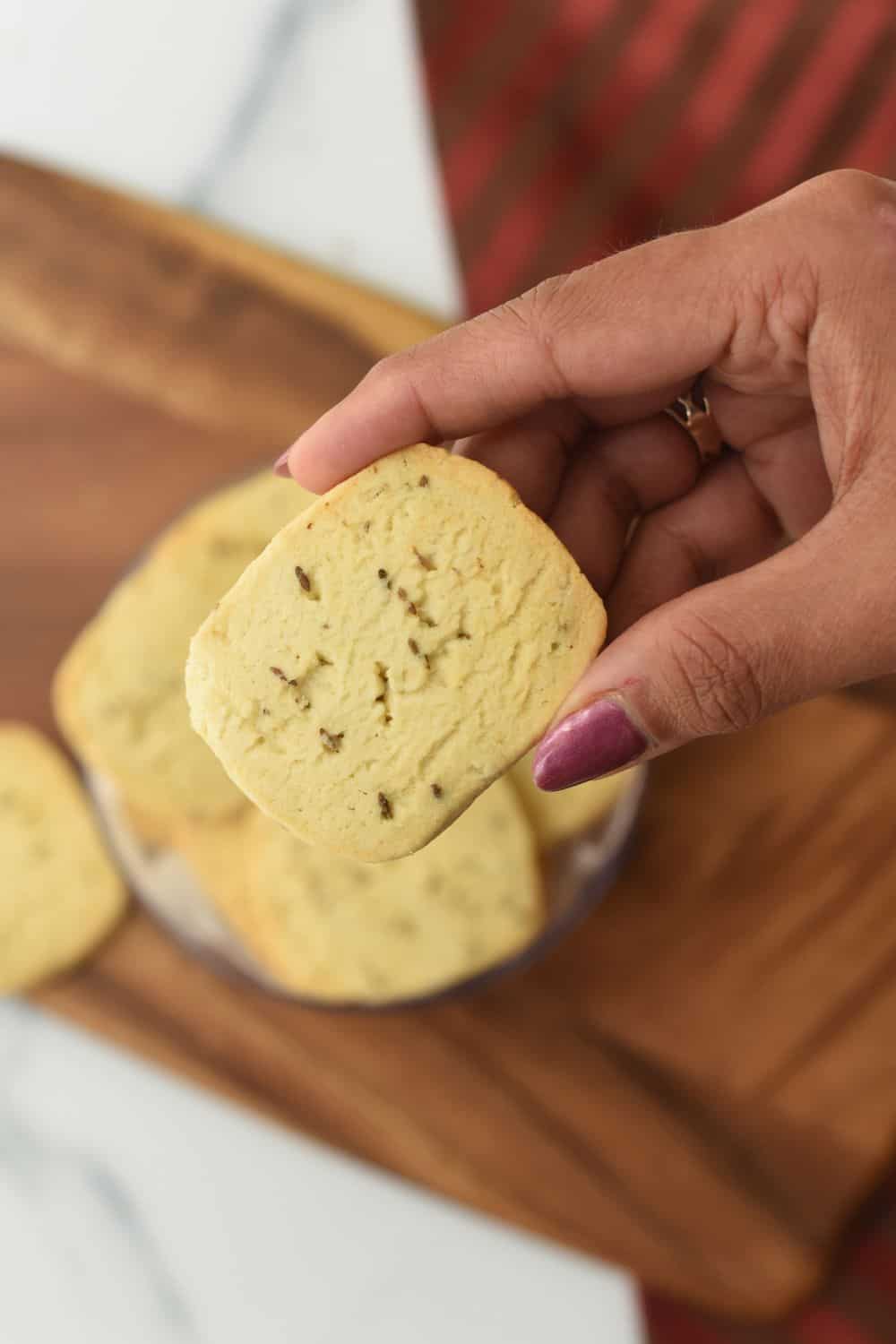 Close-up of a hand holding a soft, homemade jeera biscuit for tea.