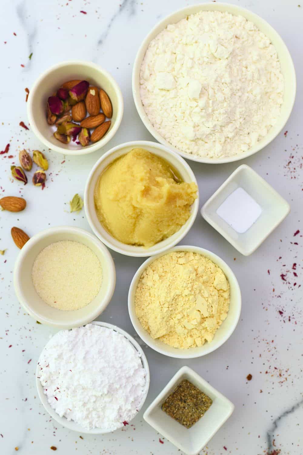 Assorted ingredients for eggless Nankhatai cookies on a white surface.